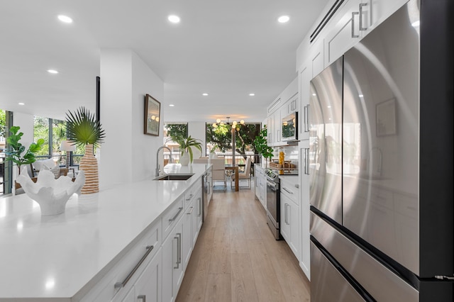 kitchen with appliances with stainless steel finishes, white cabinetry, sink, and light hardwood / wood-style flooring