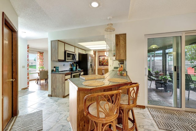 kitchen with a kitchen breakfast bar, kitchen peninsula, tile countertops, a textured ceiling, and appliances with stainless steel finishes