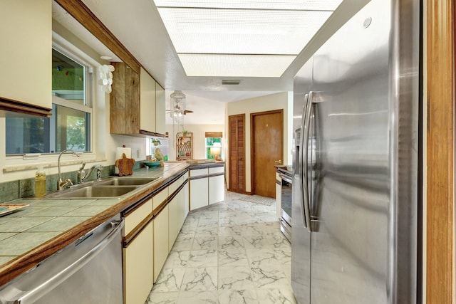 kitchen featuring tile countertops, sink, decorative light fixtures, white cabinetry, and stainless steel appliances