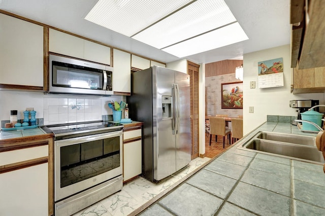 kitchen featuring tile countertops, sink, tasteful backsplash, white cabinetry, and stainless steel appliances