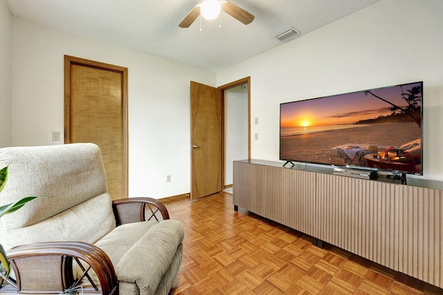 living area with a textured ceiling, light parquet flooring, and ceiling fan