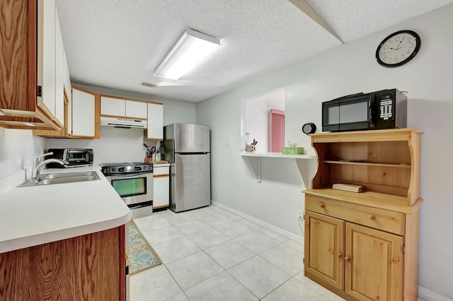 kitchen with appliances with stainless steel finishes, a textured ceiling, sink, and light tile patterned floors