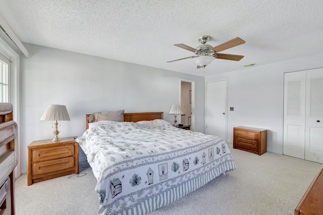 bedroom with a closet, a textured ceiling, light colored carpet, and ceiling fan