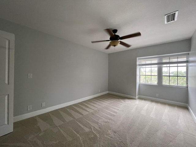 carpeted spare room featuring baseboards, a ceiling fan, and visible vents