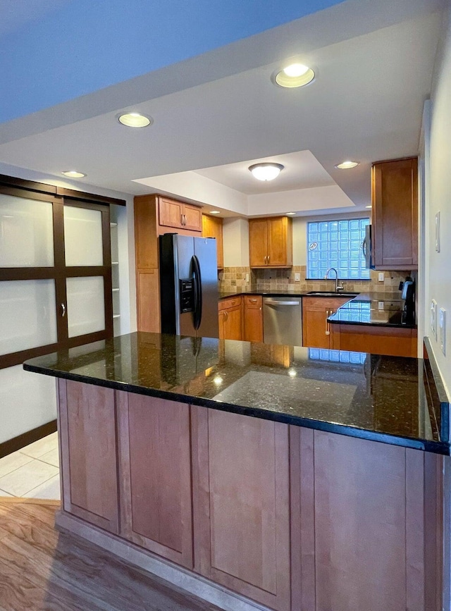 kitchen featuring dark stone countertops, light hardwood / wood-style flooring, stainless steel appliances, and kitchen peninsula