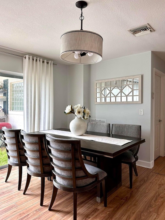 dining room with light wood-type flooring, visible vents, and a textured ceiling