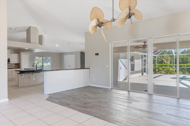 unfurnished living room with light wood-type flooring, ceiling fan, and a high ceiling