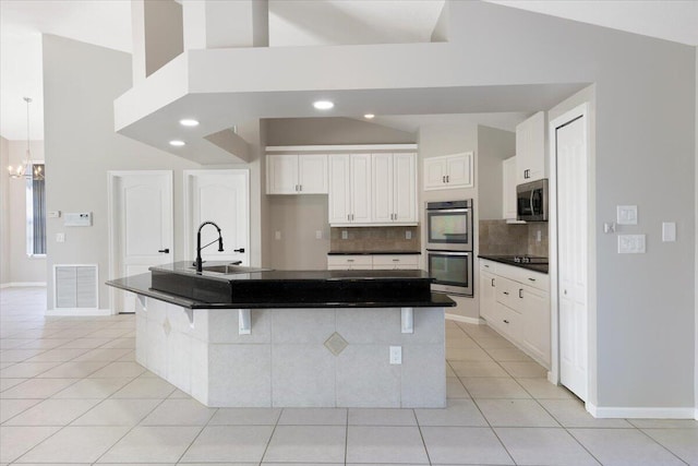 kitchen featuring appliances with stainless steel finishes, light tile patterned flooring, white cabinetry, a breakfast bar area, and a center island with sink