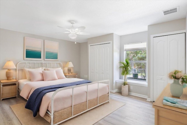 bedroom featuring ceiling fan, multiple closets, and light hardwood / wood-style flooring