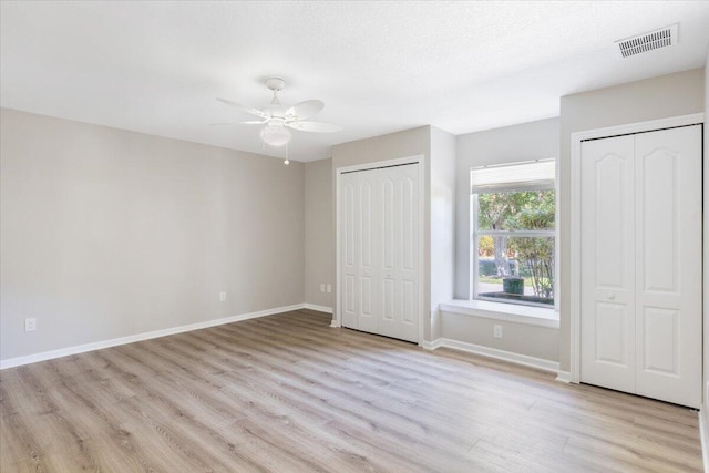 unfurnished bedroom with a textured ceiling, ceiling fan, multiple closets, and light hardwood / wood-style flooring