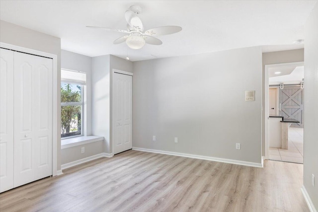 unfurnished bedroom with light hardwood / wood-style flooring, ceiling fan, and a barn door