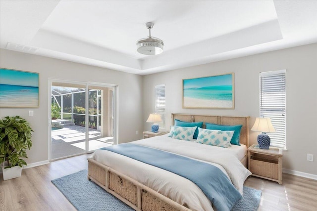 bedroom featuring access to outside, a raised ceiling, and light hardwood / wood-style floors