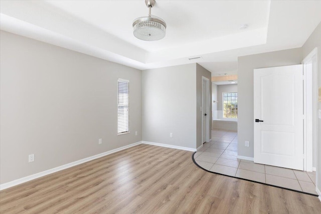 empty room featuring light wood-type flooring and a tray ceiling