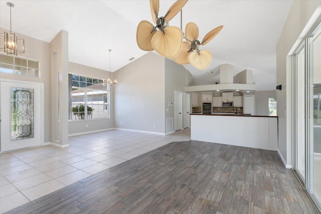 unfurnished living room featuring light hardwood / wood-style floors, sink, ceiling fan, and high vaulted ceiling