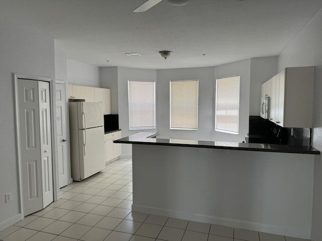 kitchen with white appliances, kitchen peninsula, white cabinetry, and light tile patterned flooring