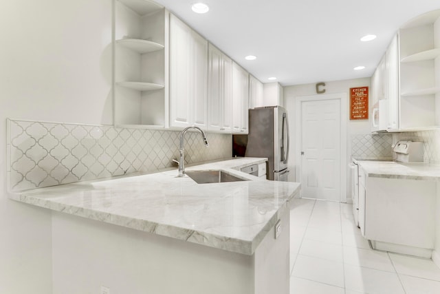 kitchen with stainless steel fridge, range, white cabinetry, light stone counters, and kitchen peninsula