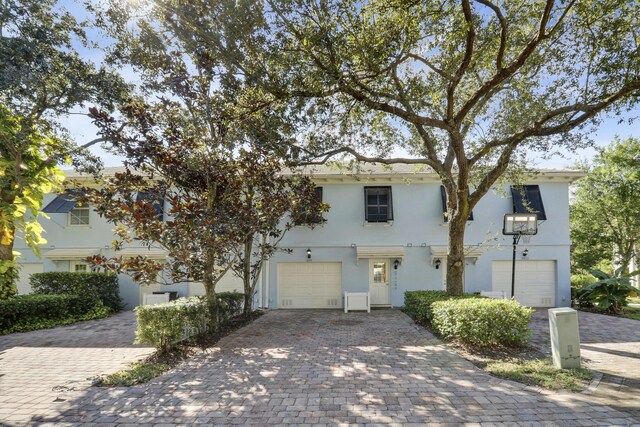 view of front facade with stucco siding, an attached garage, and decorative driveway