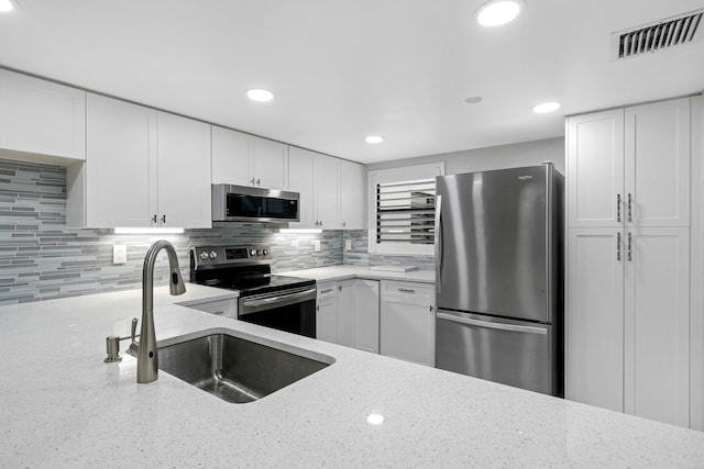 kitchen with sink, appliances with stainless steel finishes, light stone countertops, white cabinets, and decorative backsplash