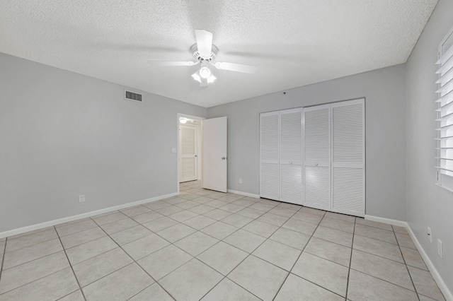 unfurnished bedroom with light tile patterned floors, ceiling fan, a textured ceiling, and a closet