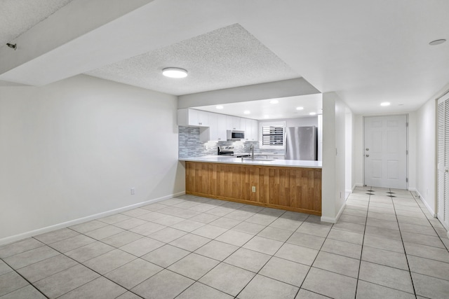 kitchen featuring light tile patterned flooring, white cabinetry, kitchen peninsula, appliances with stainless steel finishes, and a textured ceiling