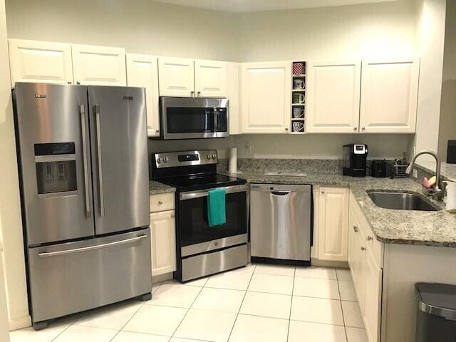 kitchen with white cabinets, appliances with stainless steel finishes, light tile patterned floors, and light stone countertops