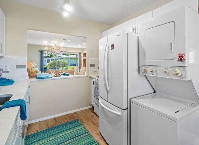 washroom with an inviting chandelier, light hardwood / wood-style flooring, stacked washer / dryer, and a textured ceiling