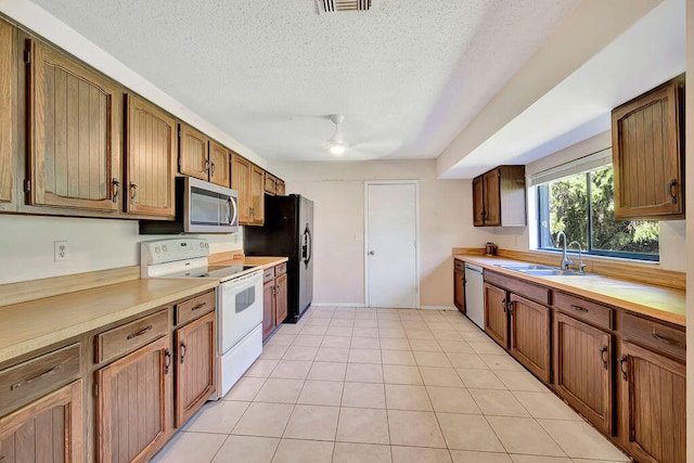 kitchen with sink, light tile patterned flooring, stainless steel appliances, and a textured ceiling