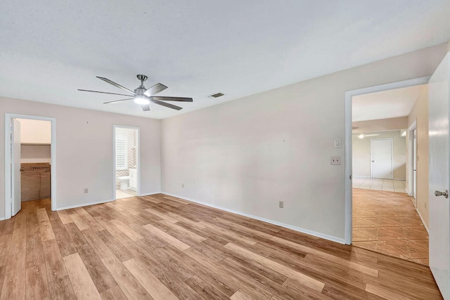 unfurnished bedroom featuring a spacious closet, light hardwood / wood-style flooring, ensuite bathroom, and ceiling fan