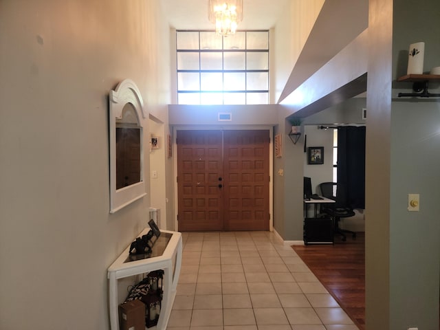 foyer entrance with a towering ceiling, a chandelier, and light tile patterned flooring