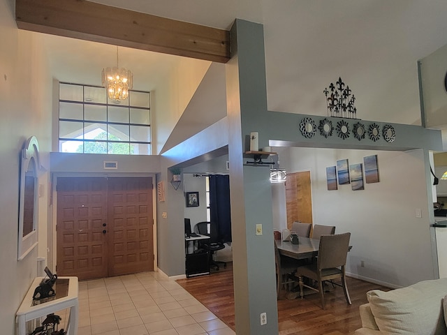 foyer entrance with light wood-type flooring, a high ceiling, beam ceiling, and a chandelier