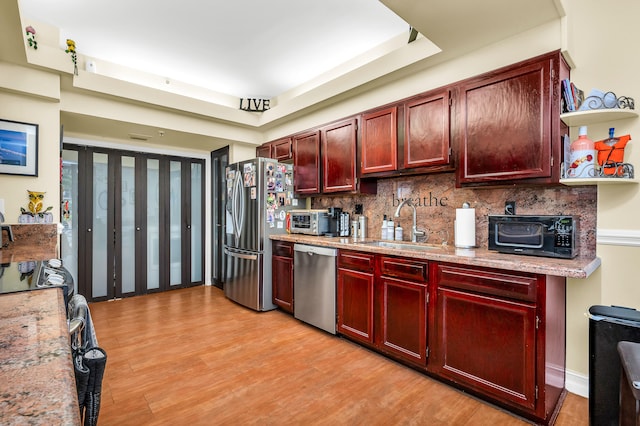 kitchen featuring backsplash, a tray ceiling, appliances with stainless steel finishes, and light hardwood / wood-style flooring