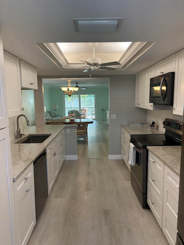 kitchen featuring light stone countertops, black appliances, white cabinetry, sink, and a tray ceiling