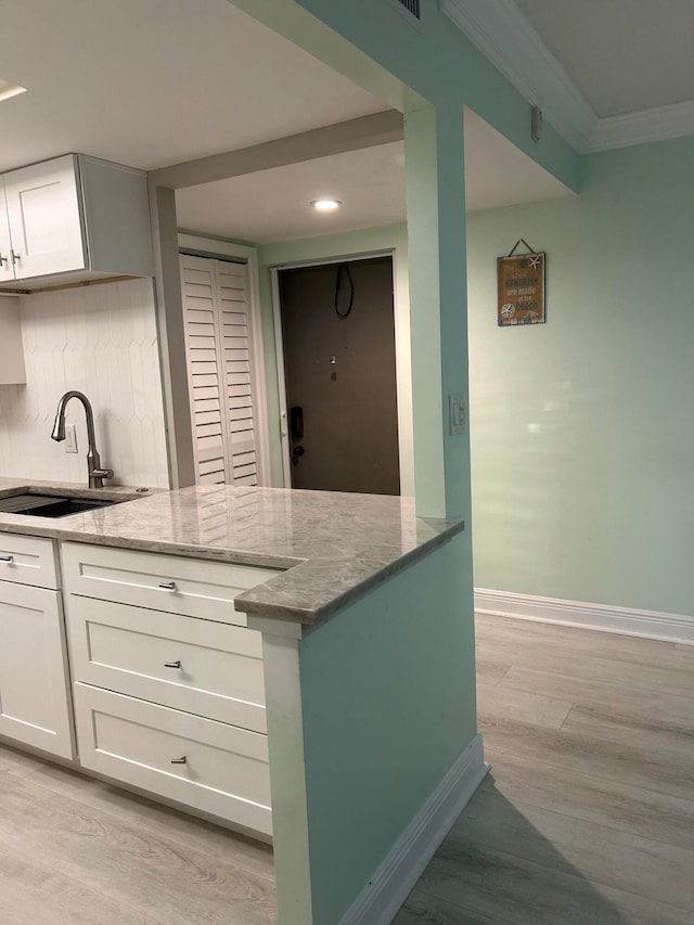 kitchen with light stone countertops, light hardwood / wood-style floors, decorative backsplash, white cabinets, and sink