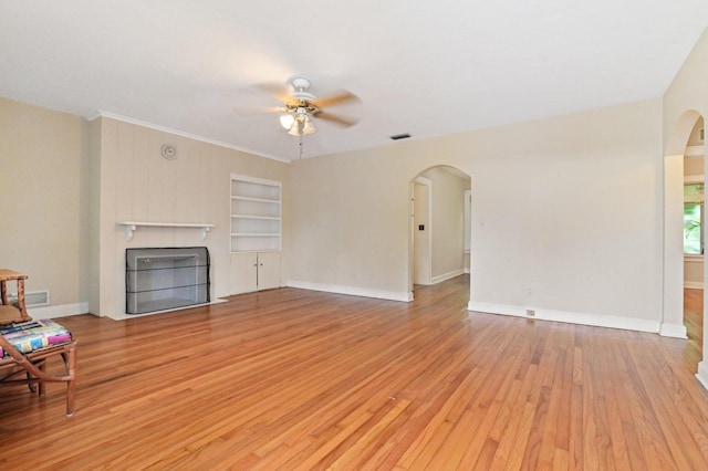 living room with light hardwood / wood-style floors, a fireplace, crown molding, ceiling fan, and built in shelves