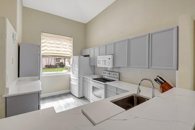 kitchen with light stone counters, gray cabinets, a sink, white appliances, and baseboards