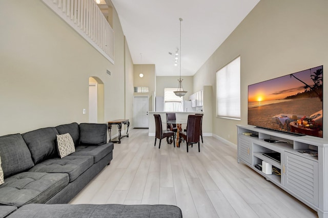 living area with baseboards, arched walkways, visible vents, a towering ceiling, and light wood-type flooring