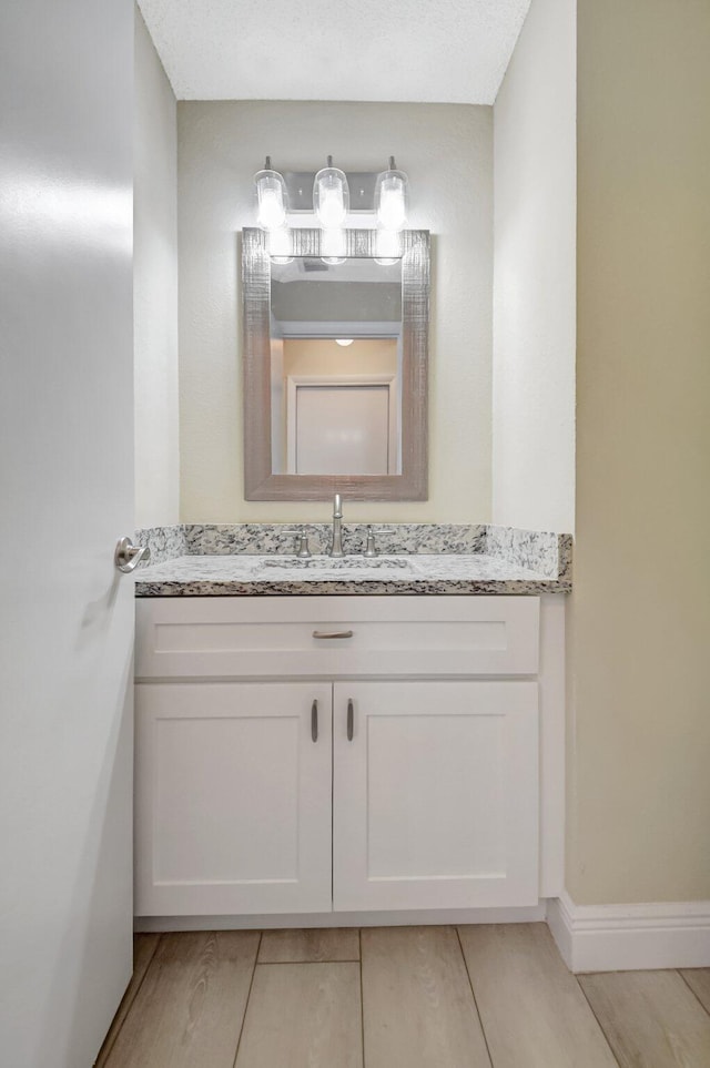 bathroom with a textured ceiling, vanity, and baseboards