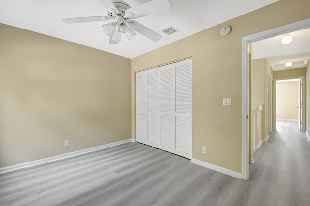 unfurnished bedroom featuring a closet, visible vents, a ceiling fan, wood finished floors, and baseboards