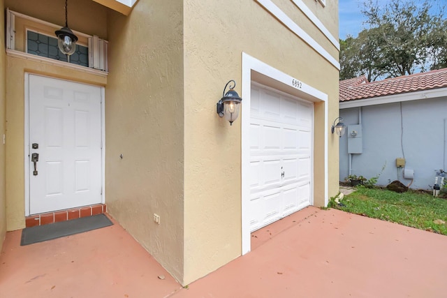 property entrance featuring a garage, a tiled roof, and stucco siding