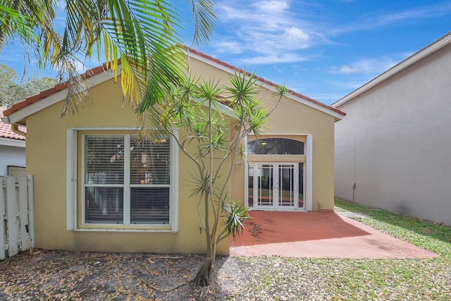 rear view of house featuring french doors, a patio area, fence, and stucco siding