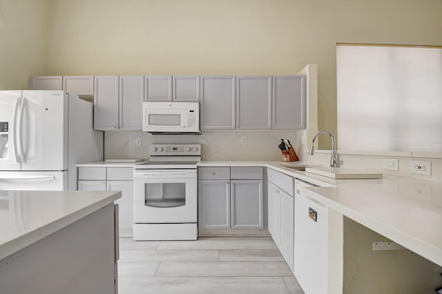 kitchen with gray cabinets, white appliances, light countertops, and a sink