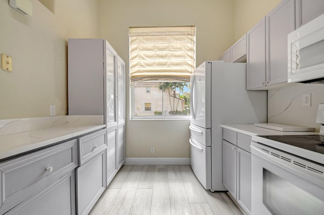 kitchen featuring white appliances, baseboards, light wood-type flooring, gray cabinets, and light stone countertops