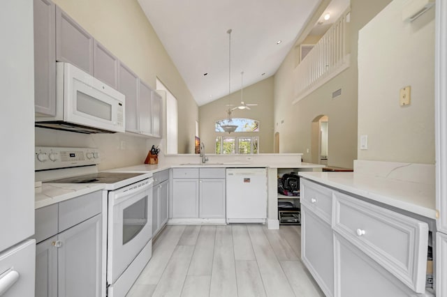 kitchen with a peninsula, white appliances, a sink, light stone countertops, and pendant lighting