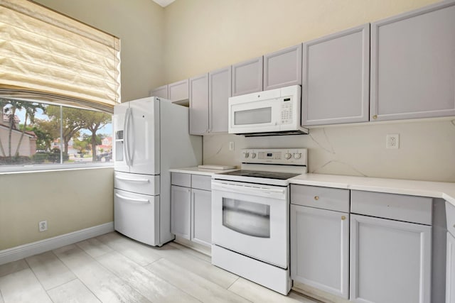 kitchen featuring white appliances, baseboards, gray cabinets, and light countertops