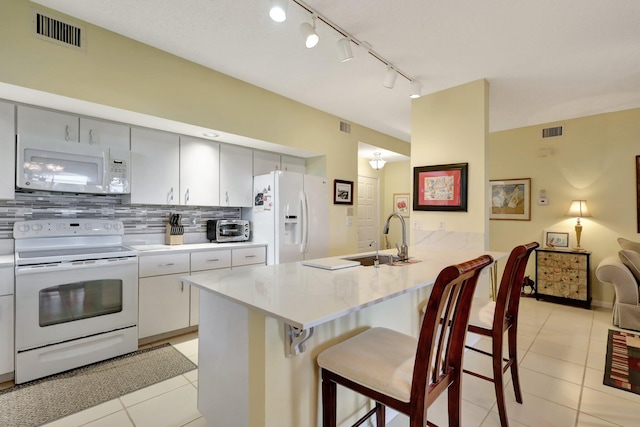 kitchen featuring white appliances, sink, light tile patterned floors, tasteful backsplash, and a kitchen bar