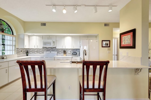 kitchen featuring a kitchen breakfast bar, kitchen peninsula, decorative backsplash, and white appliances