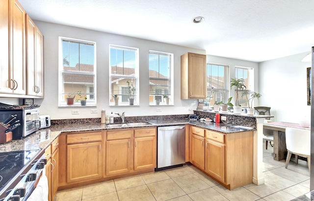 kitchen featuring light tile patterned flooring, sink, kitchen peninsula, stainless steel appliances, and dark stone countertops