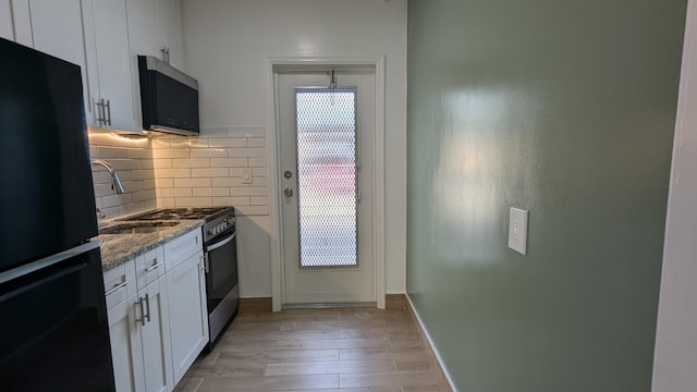 kitchen featuring light hardwood / wood-style floors, white cabinets, decorative backsplash, appliances with stainless steel finishes, and dark stone countertops