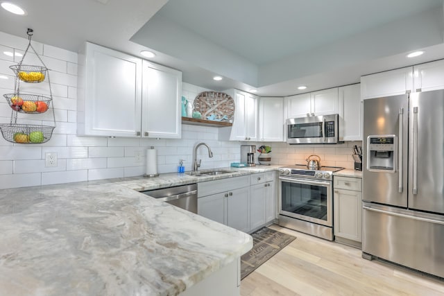 kitchen with light wood-type flooring, sink, stainless steel appliances, hanging light fixtures, and white cabinets