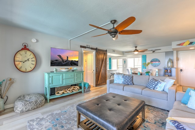 living room with ceiling fan, a barn door, light hardwood / wood-style floors, and a textured ceiling